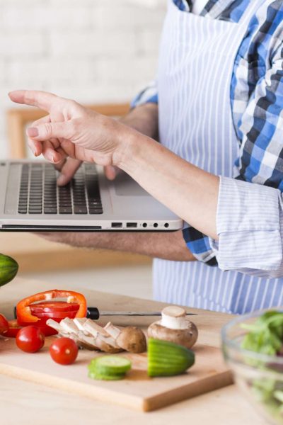 close-up-senior-woman-pointing-laptop-hold-by-her-husband-while-preparing-vegetable-salad
